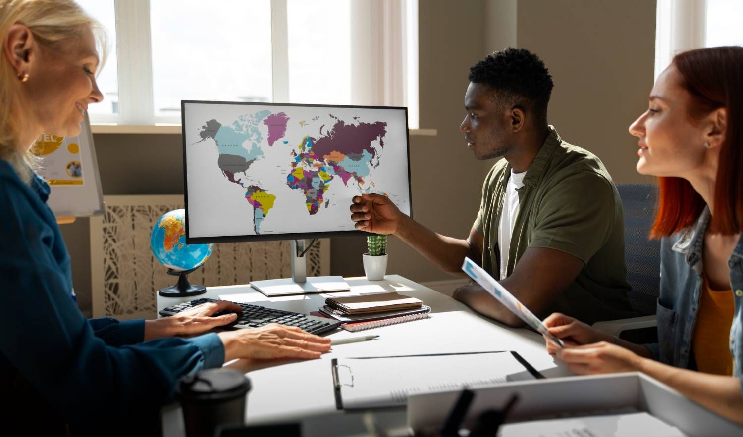 Team analyzing a world map on a computer screen, possibly discussing international business companies (IBCs).