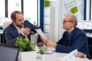 Business meeting: Two men review charts at a table in an office setting.