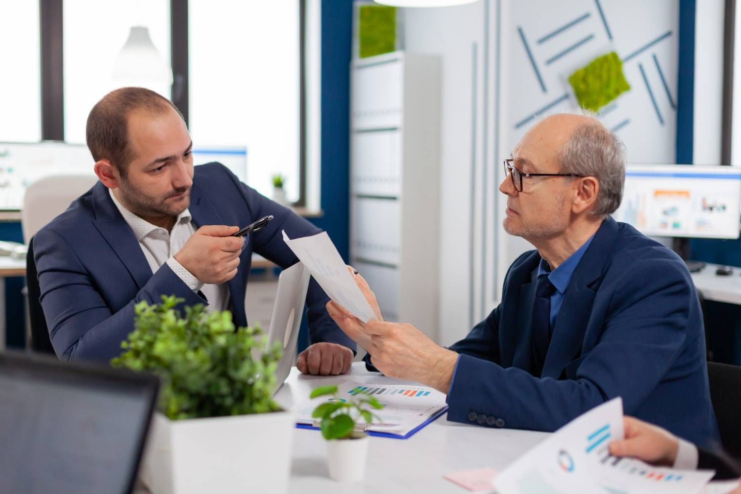 Business meeting: Two men review charts at a table in an office setting.