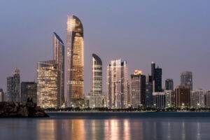 Abu Dhabi skyline at dusk, showing modern buildings reflected in the water.