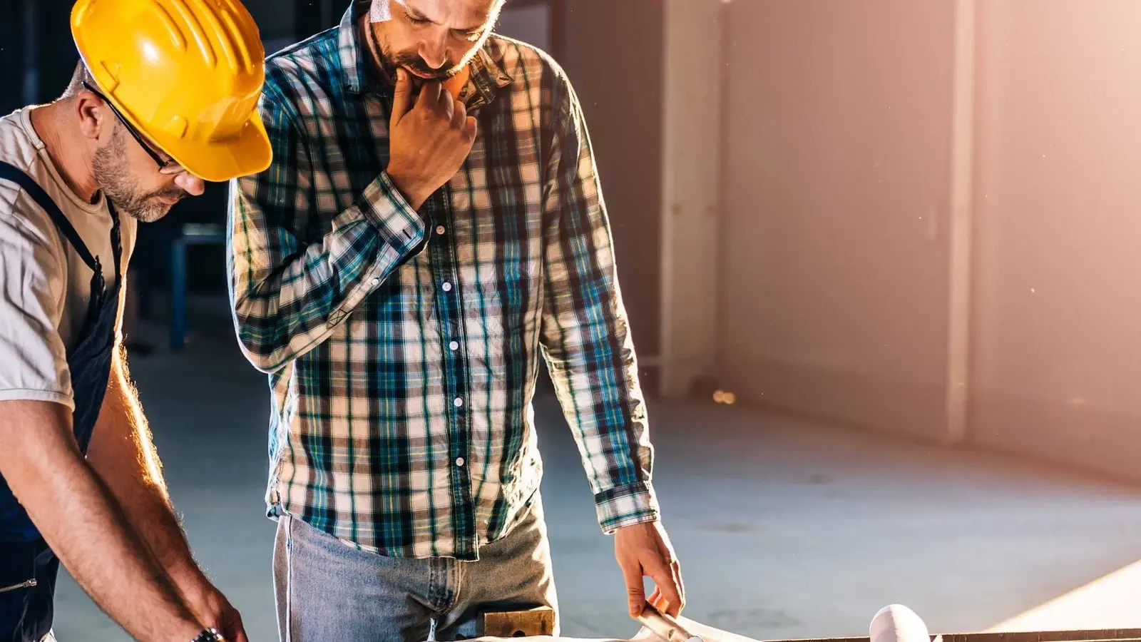 Two construction workers review blueprints, discussing building defects and shared responsibility.