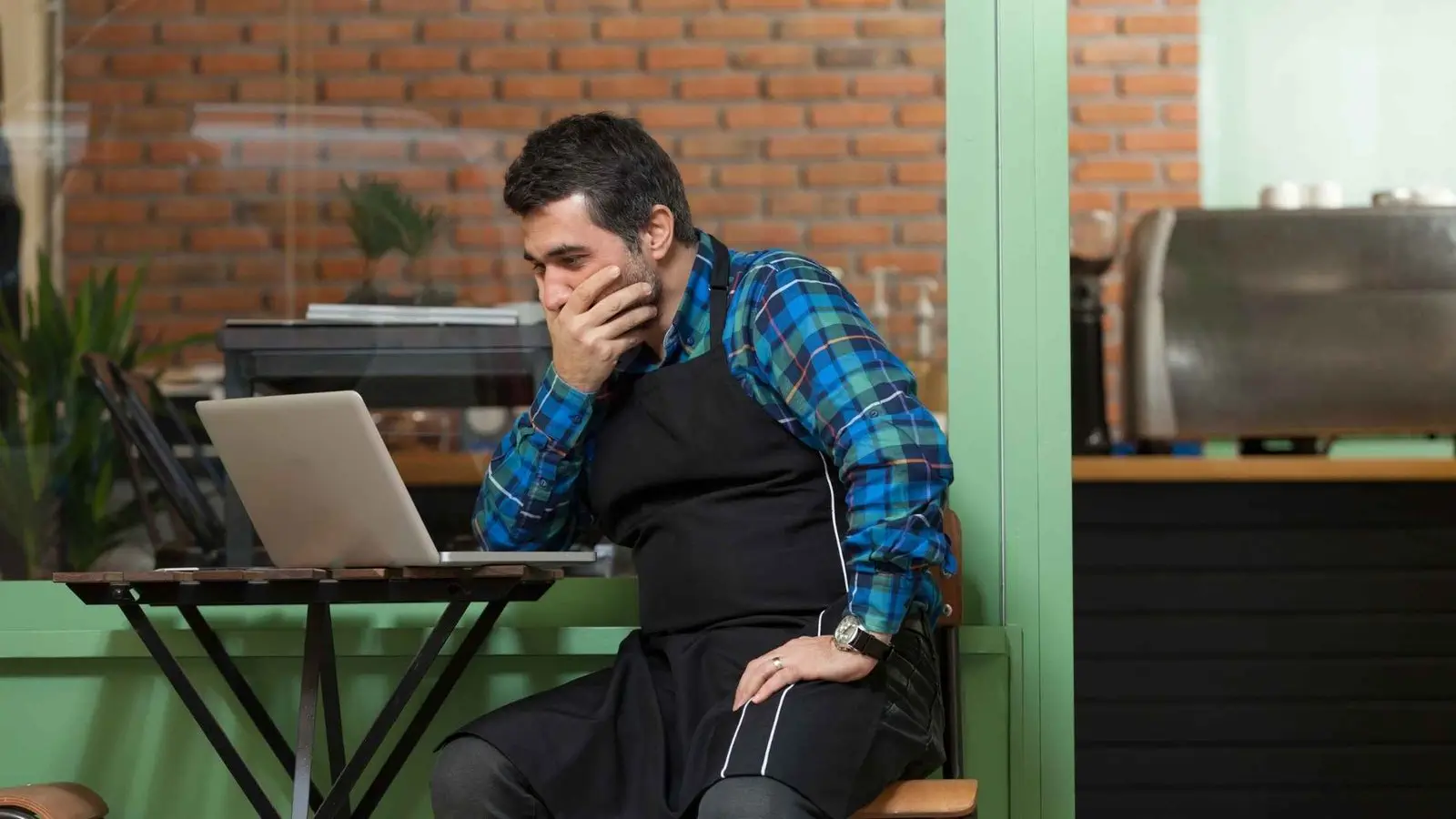 Stressed business owner reviewing laptop, seeking strategic advice.