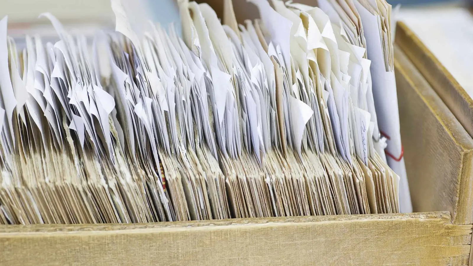 Close-up of old, well-used paper files organized in a wooden box, with numerous papers sticking out.