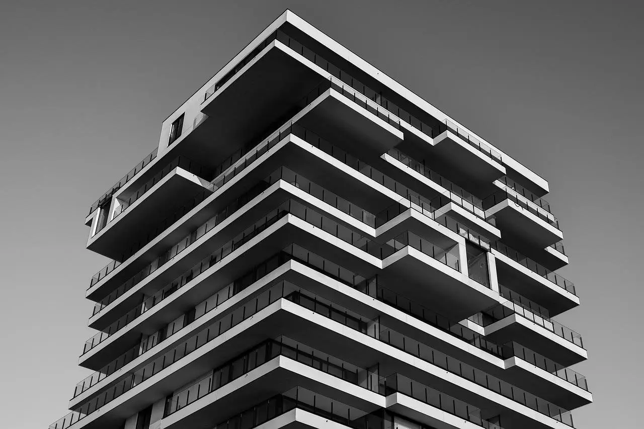 Modern high-rise building with staggered balconies and glass railings, captured in black and white from a low angle against a clear sky.