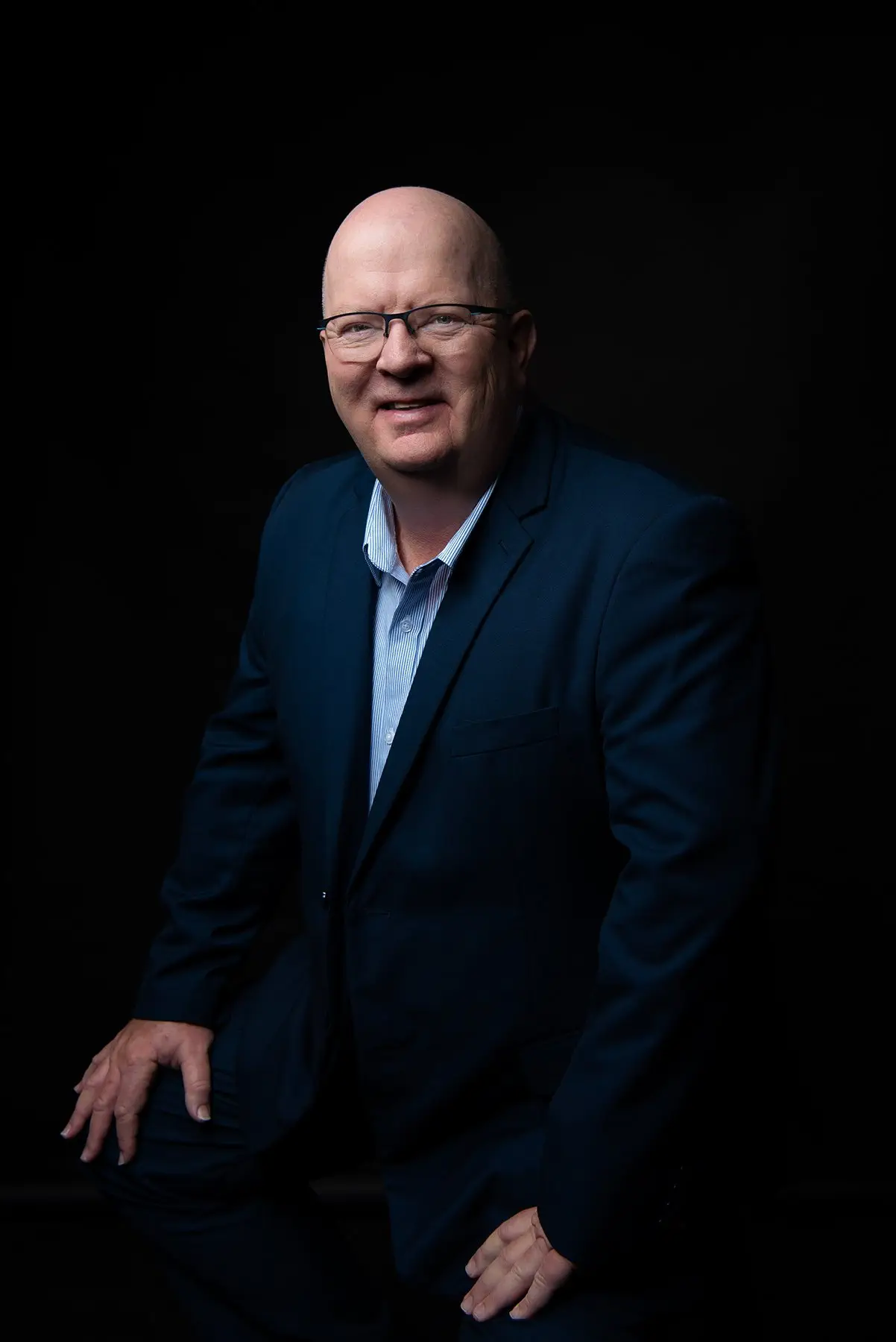 Smiling bald man in a dark blue suit and glasses