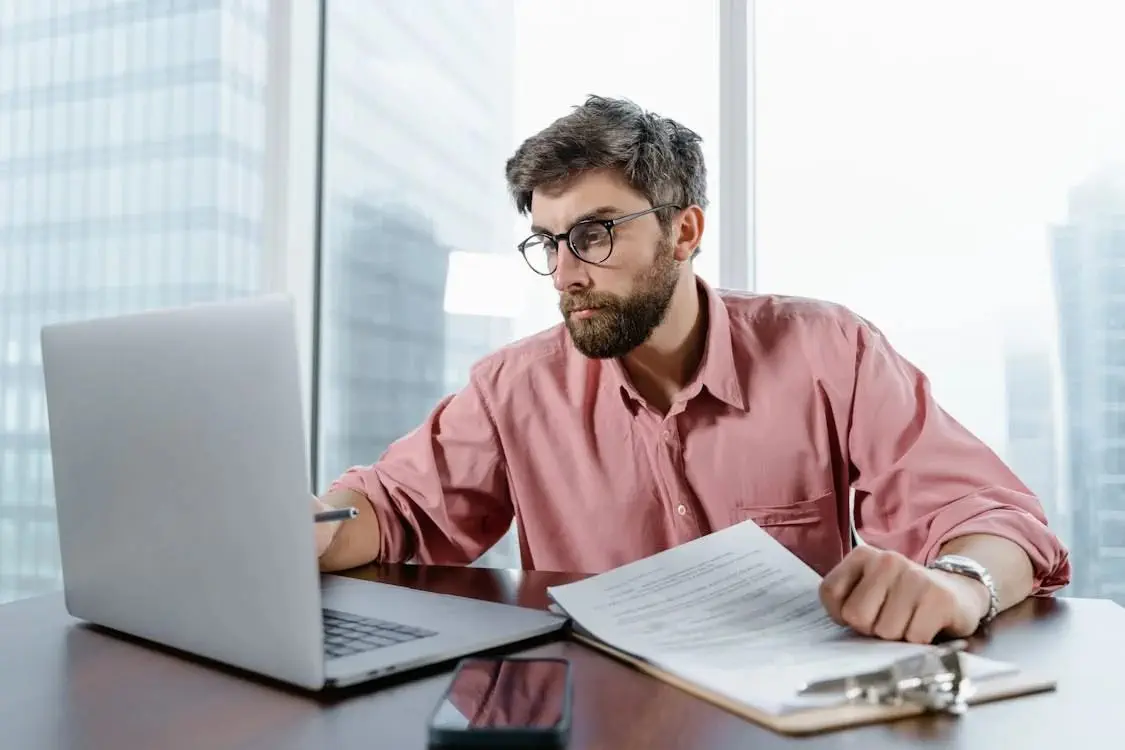 Man in office using laptop, reviewing tax residence test documents.