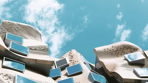 Wavy architectural building with irregularly placed windows under a blue sky with scattered clouds.