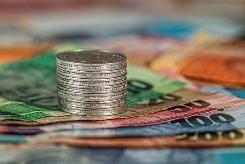 Stack of silver coins on top of colorful banknotes.