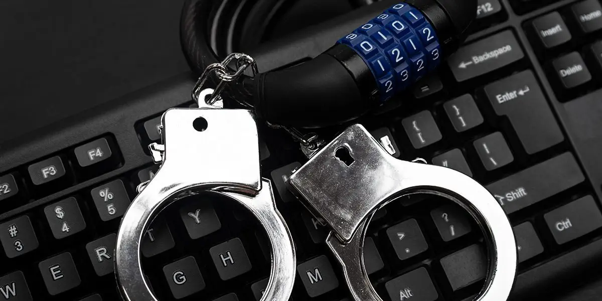 Handcuffs and a combination lock on a keyboard; cyber attack prevention.