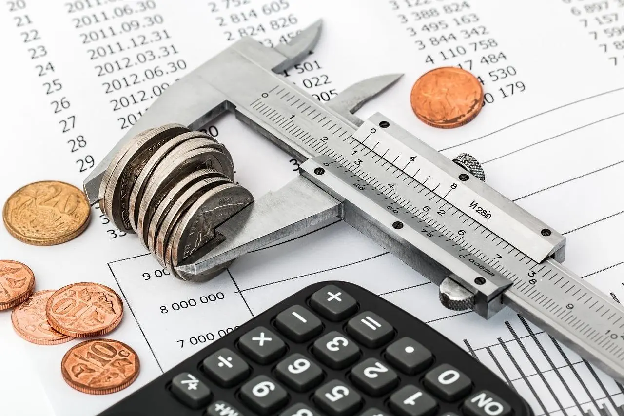 Close-up of a caliper measuring coins, placed on a financial document with a black calculator and scattered coins in the background.