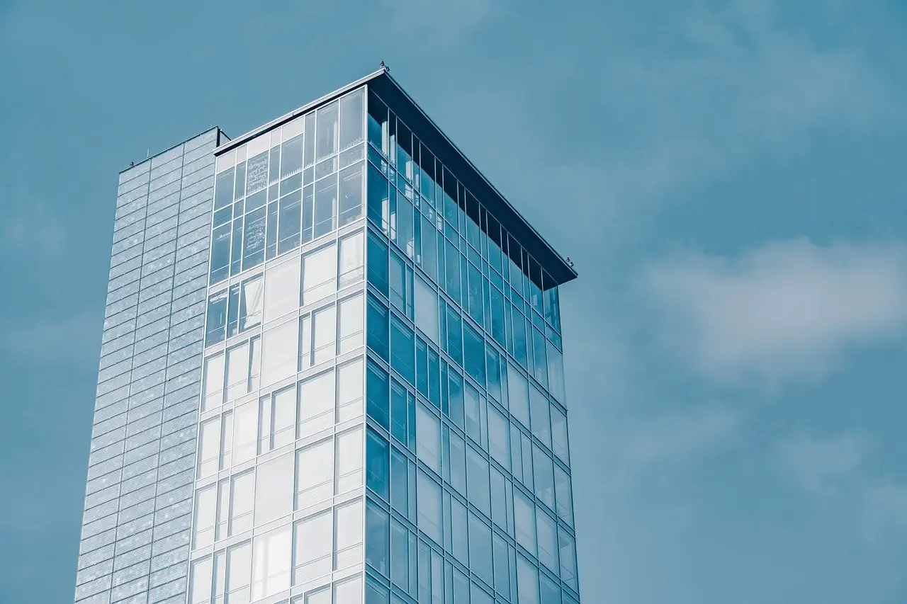 Glass high-rise building against a blue sky with scattered clouds.