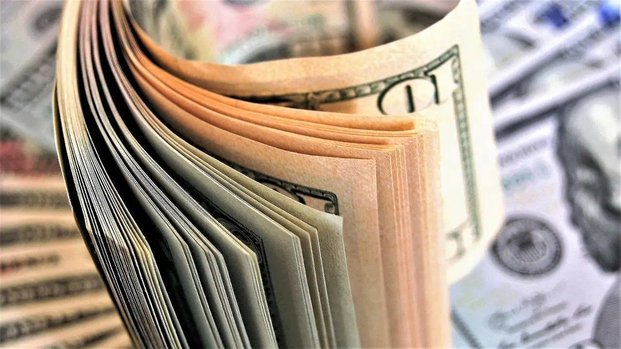 Close-up stack of clean and crisp one hundred dollar bills fanned out on top of more U.S. currency.