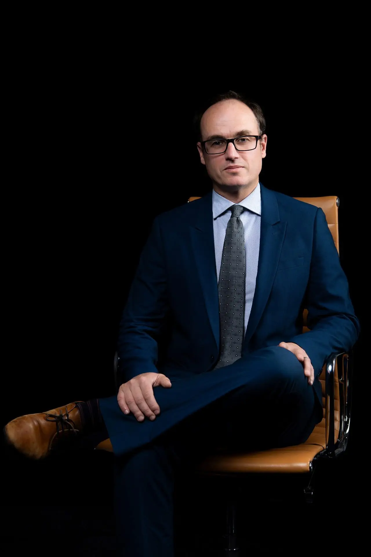 Iain Mark sits in an office chair, wearing a suit and glasses.