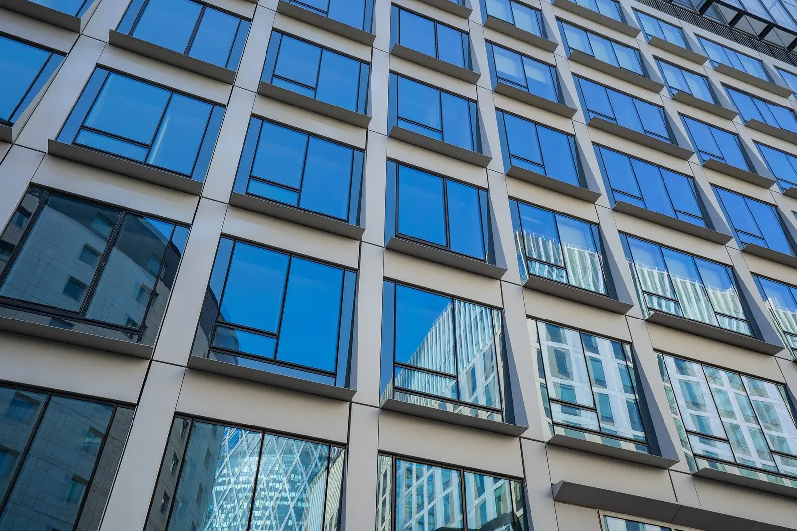 Glass office building facade with blue sky reflecting in the windows, creating a grid-like pattern.