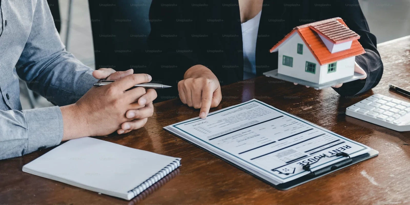 Two people discuss estate planning, reviewing documents and holding a house model, to avoid common mistakes.