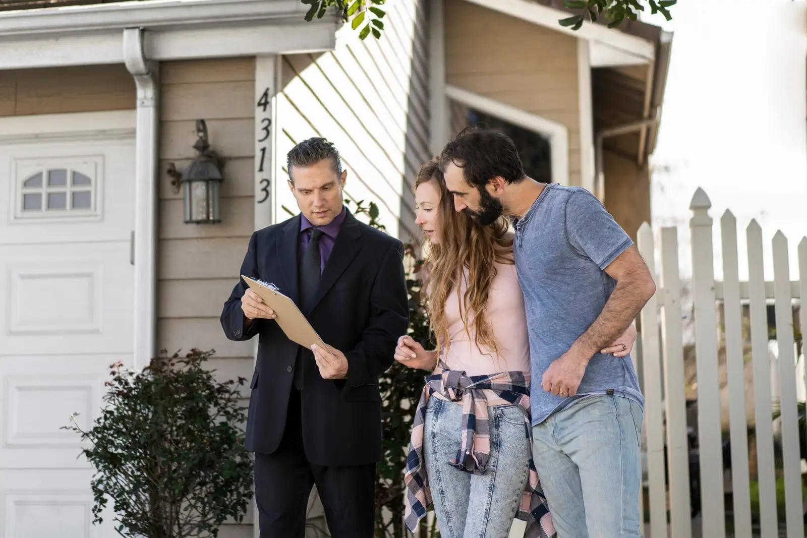 Real estate agent discusses paperwork with a couple outside a house.